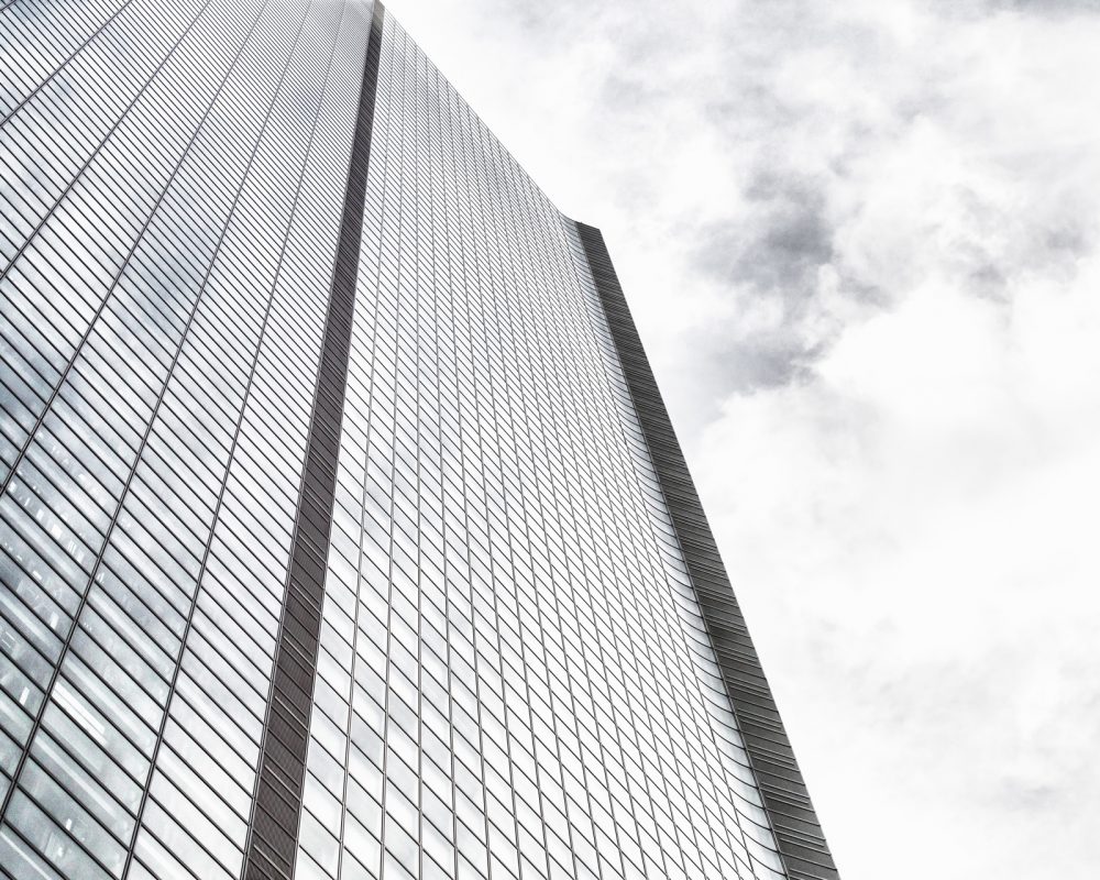 Low angle shot of a modern glass skyscraper on a cloudy sky background A low angle shot of a modern glass skyscraper on a cloudy sky background
